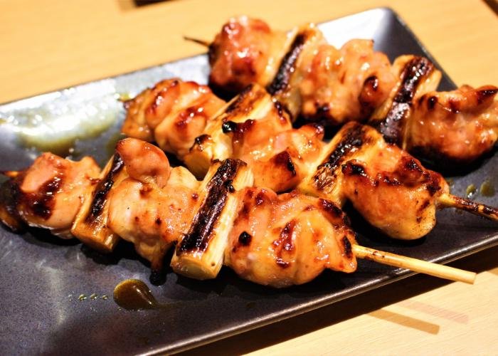 Yakitori chicken on skewers on black square dish, grilled in brown sauce