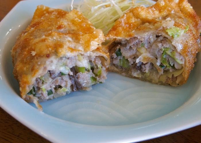 Cut open gyoza fried potsticker filled with meat and green vegetables on light blue dish