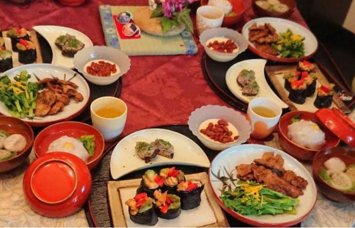 Table filled with food on different plates and dishes, including sushi, chicken, rice, vegetables