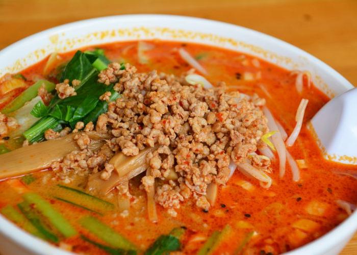 Red broth in white bowl topped with diced onions and chives, spoon