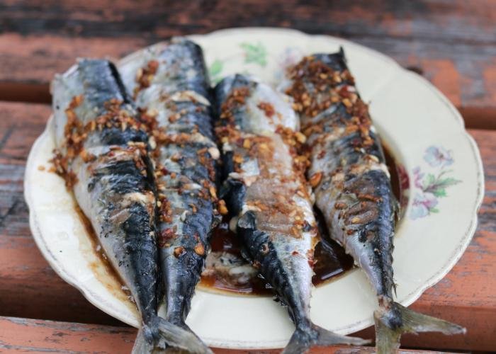Four sardines with brown sauce and sesame seeds on white dish with flowers printed on it