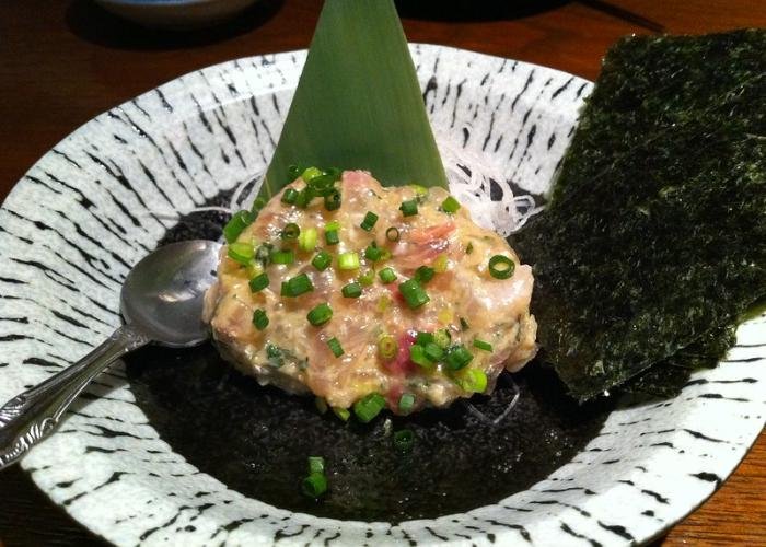 Clump of beige minced fish meat with soybean paste, topped with green onions, on top of seaweed with spoon