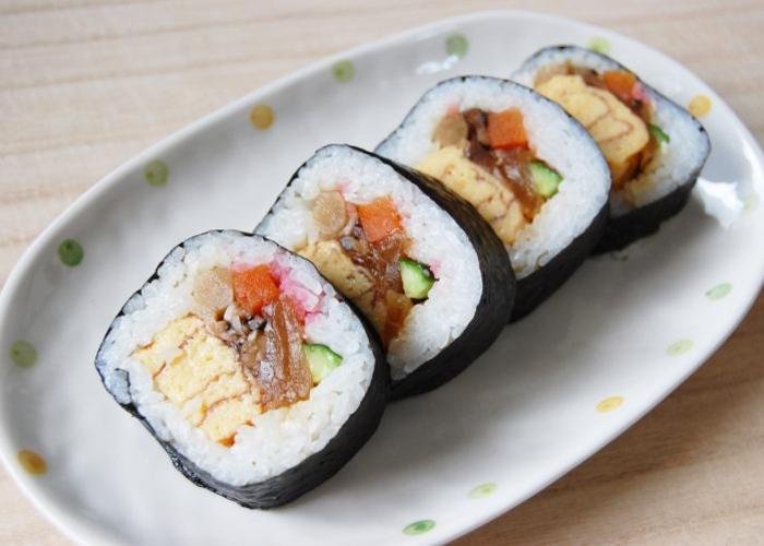 Large cut pieces of rolled sushi with colorful egg, vegetables, and meat in middle on white dish