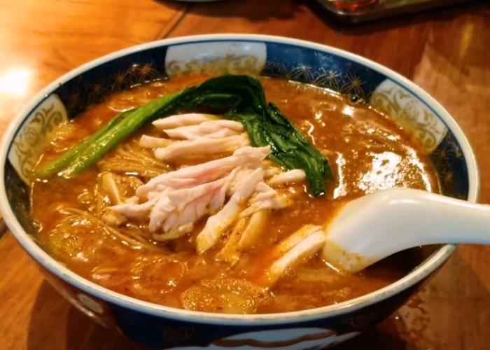 Tantanmen ramen bowl with red broth, spices, with vegetables and white soup spoon