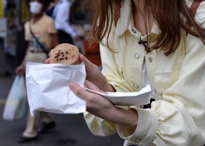 Woman dressed in yellow holds out an imagawayaki (Japanese sweet) from Nakano 