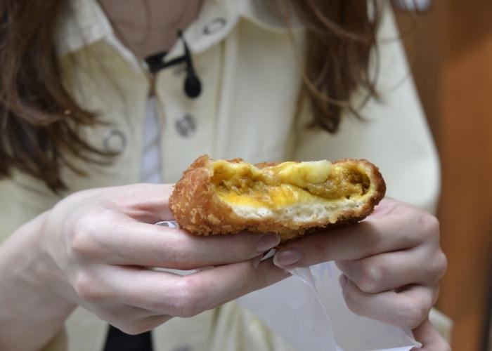 Woman holds out a Japanese karepan, curry-filled bread, which is also oozing cheese