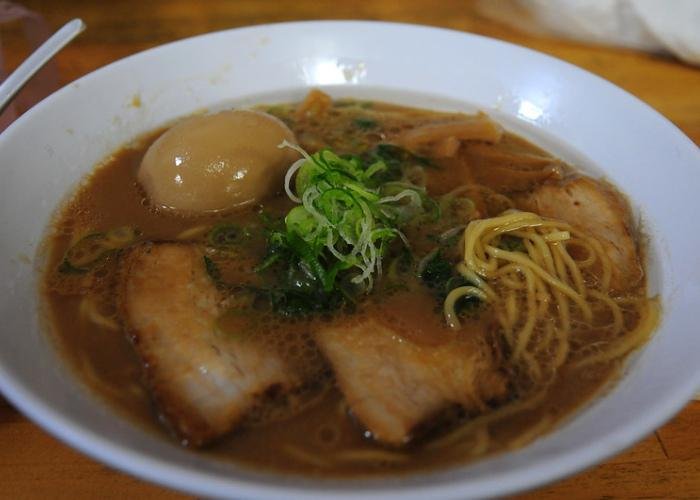 A bowl of Wakayama ramen with thick pork broth, strips of chashu, a whole boiled egg, and a topping of thinly-sliced negi