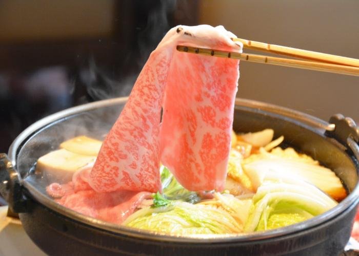 Thin slice of Japanese wagyu being dipped into a hot pot
