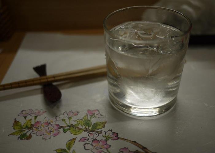 Glass of shochu on ice on a placemat decorated with sakura