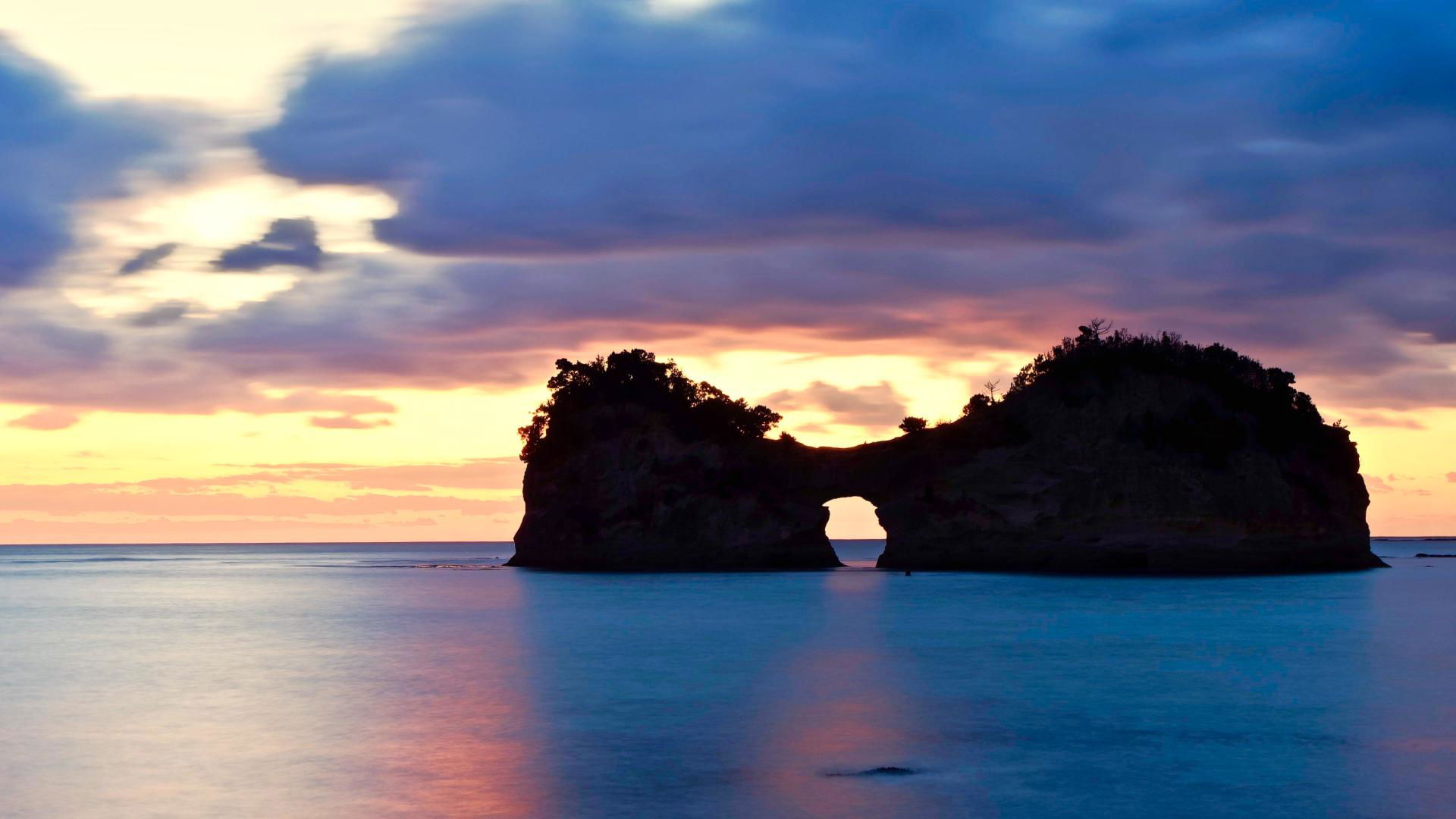 Sunset view of a rocky island silhouette over calm sea waters