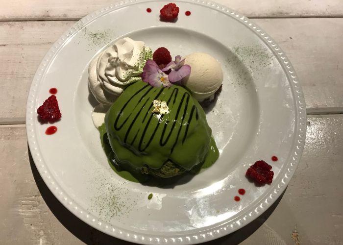 Close up shot of green matcha pancakes at Ain Soph Journey, served with ice cream and a green sauce, and topped with purple flowers