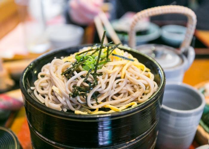 A close-up photograph of soba noodles at Honke Owariya, topped with strips of nori seaweed and light green spring onions