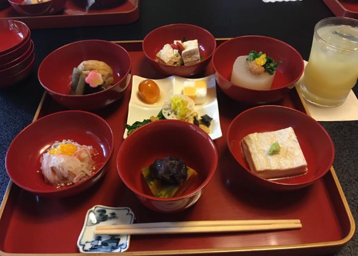 A tray with several red lacquerware dishes on it featuring various Buddhist vegetarian dishes