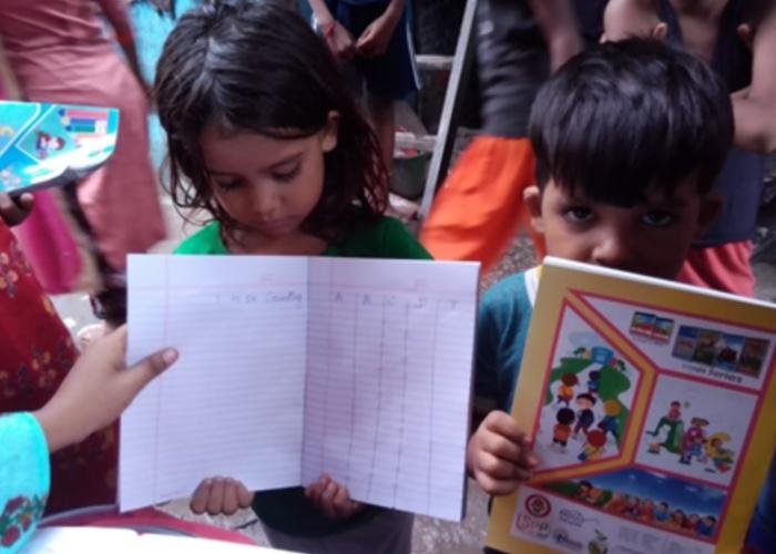 Schoolchildren hold up their homework assignments and books in India