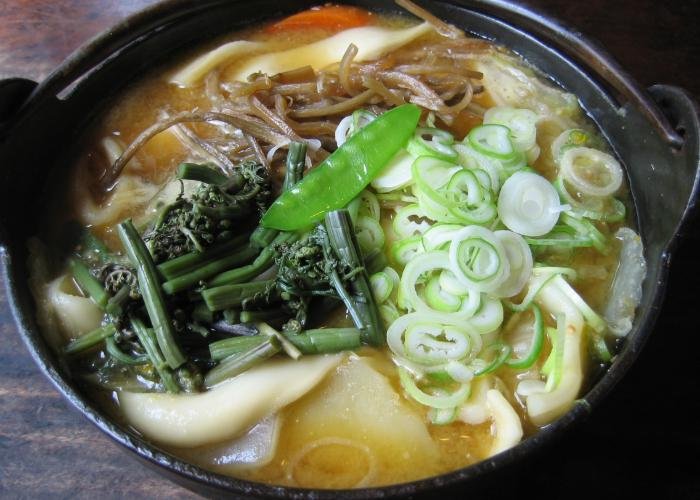 Close up image of a bowl of houtou noodles topped with vegetables