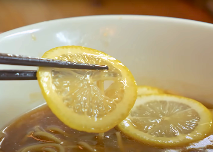 Close-up on chopsticks removing lemon slices from the lemon ramen from Rinsuzu Shokudo