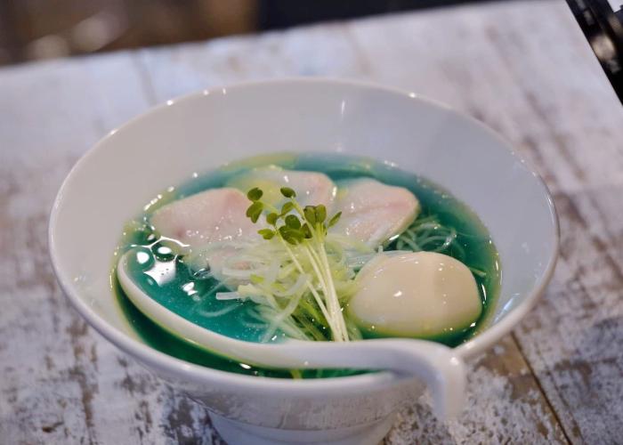 Bowl of blue ramen in Tokyo from Kipposhi, with microgreens, a whole egg, and chicken slices on top