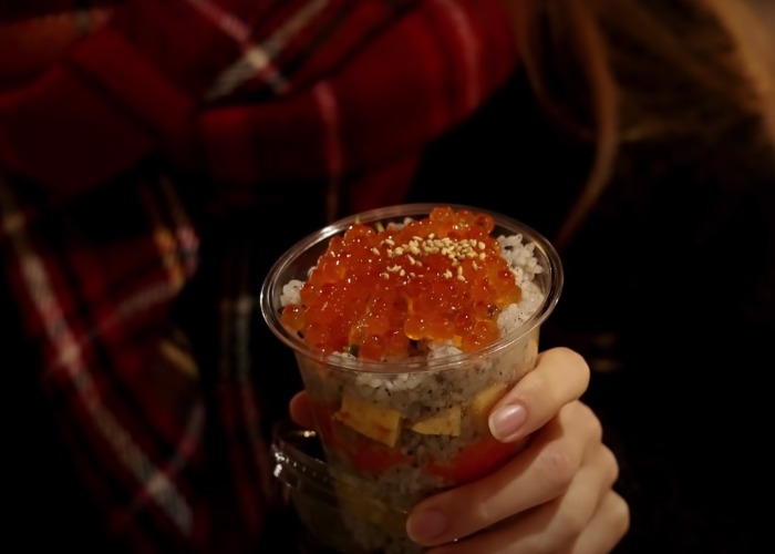A close up of Shizuka holding a cup of sushi, with salmon roe on the top