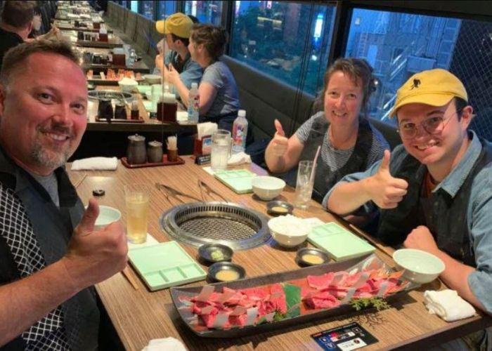 Family of three white people smiling and holding thumbs up around a yakiniku barbeque grill