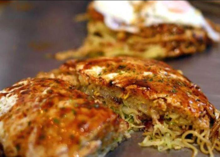 Cut-open saucy okonomiyaki Japanese pancake on a griddle with noodles inside