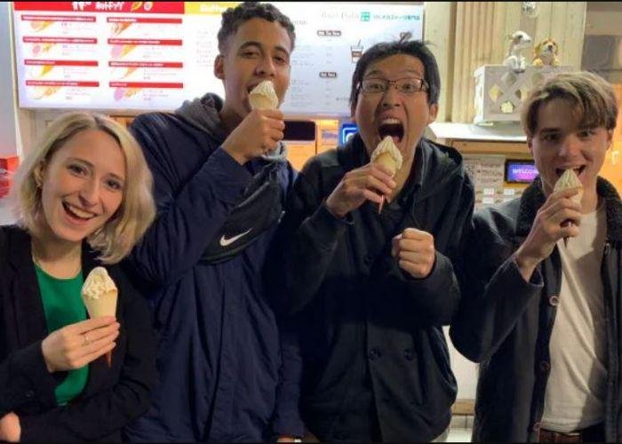 Four young people enjoying soft serve ice cream cones and making goofy faces at the camera