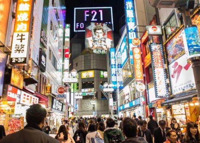 Crowd of people on busy city street with lit up ads and restaurant signs