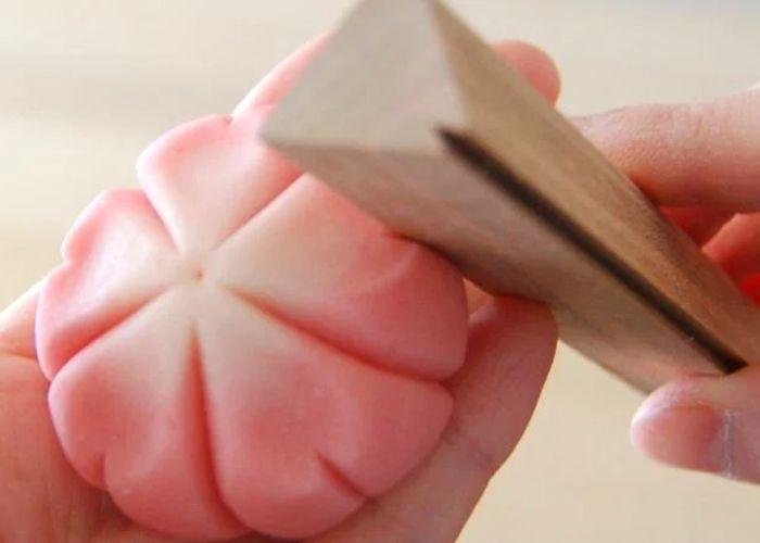 Close up of someone using a wooden tool to shape a cherry blossom wagashi sweet