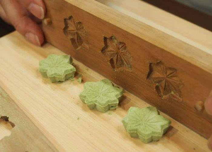 A close up image of someone popping green higashi sweets shaped like leaves out of a mold