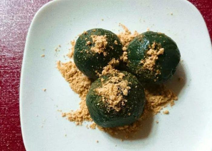 A close up shot of three green mochi covered in kinako powder on a white plate