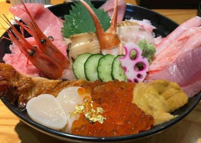 Black bowl of colorful seafood; shrimp, fish roe, cucumber, tuna piled on top of each other