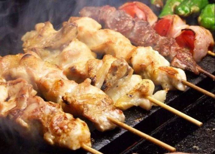 4 skewers of light meat yakitori, 2 darker red meat skewers, 1 green bell pepper skewer on grill