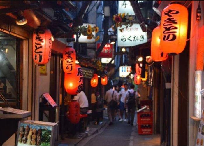 Dark street alley with hanging red lanterns saying izakaya hanging in restaurant doorways