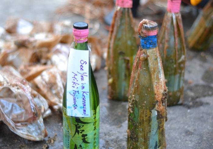 Underwater aged sake bottles with a label reading "See you in Kesennuma"