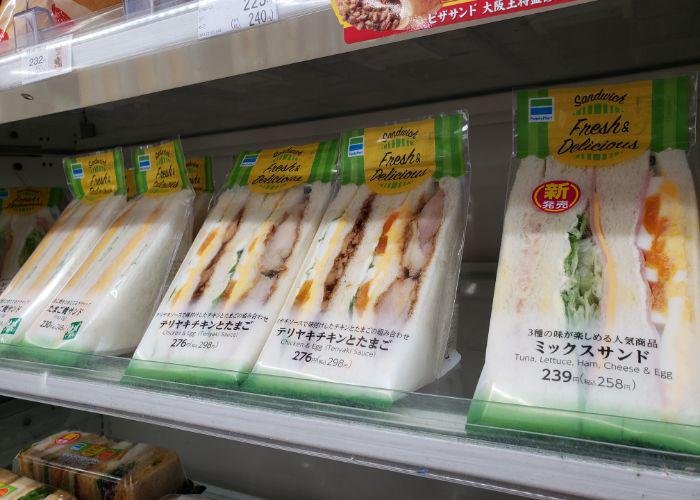 Several clear packages of two sandwiches of different varieties cut in triangles with fillings visible on convenience store shelf