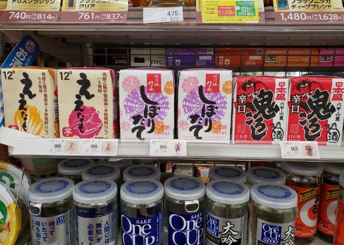Six rows of wine and sake in small square juice boxes on convenience store shelves, two with Japanese demons on them