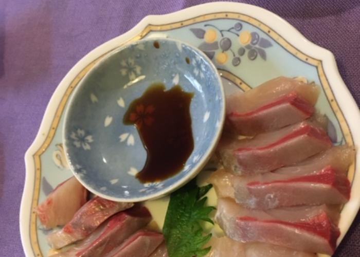 Yellowtail sashimi on a platter with a small bowl of soy sauce