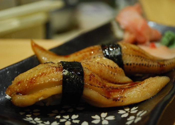 Anago (conger eel) nigiri sushi wrapped in a strip of black nori seaweed