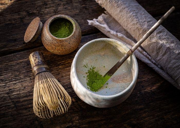 An overhead image of powdered matcha tea in a bowl, with a chasen whisk beside it