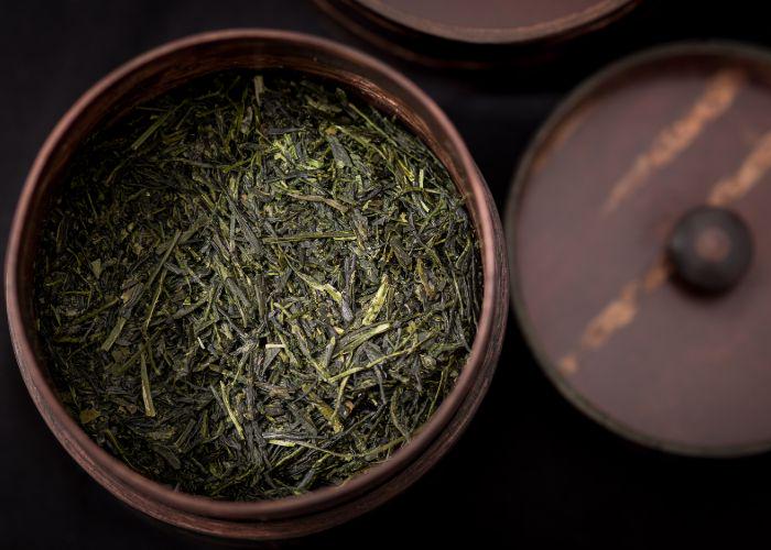 A close up image of a wooden pot full of dried, dark green gyokuro tea leaves