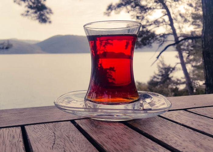 A glass of kocha tea on a wooden table, with a body of water and mountains in the background