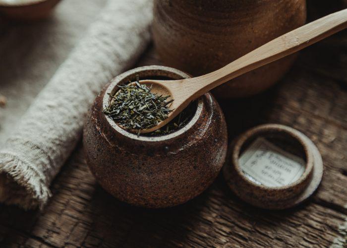 A thin wooden spoon holding dried green tea leaves