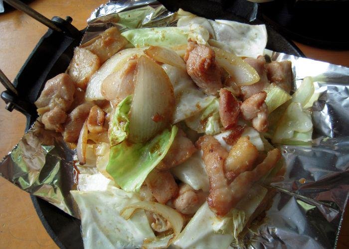 A close up image of grilled chicken with onion and cabbage, on silver foil in a black pan