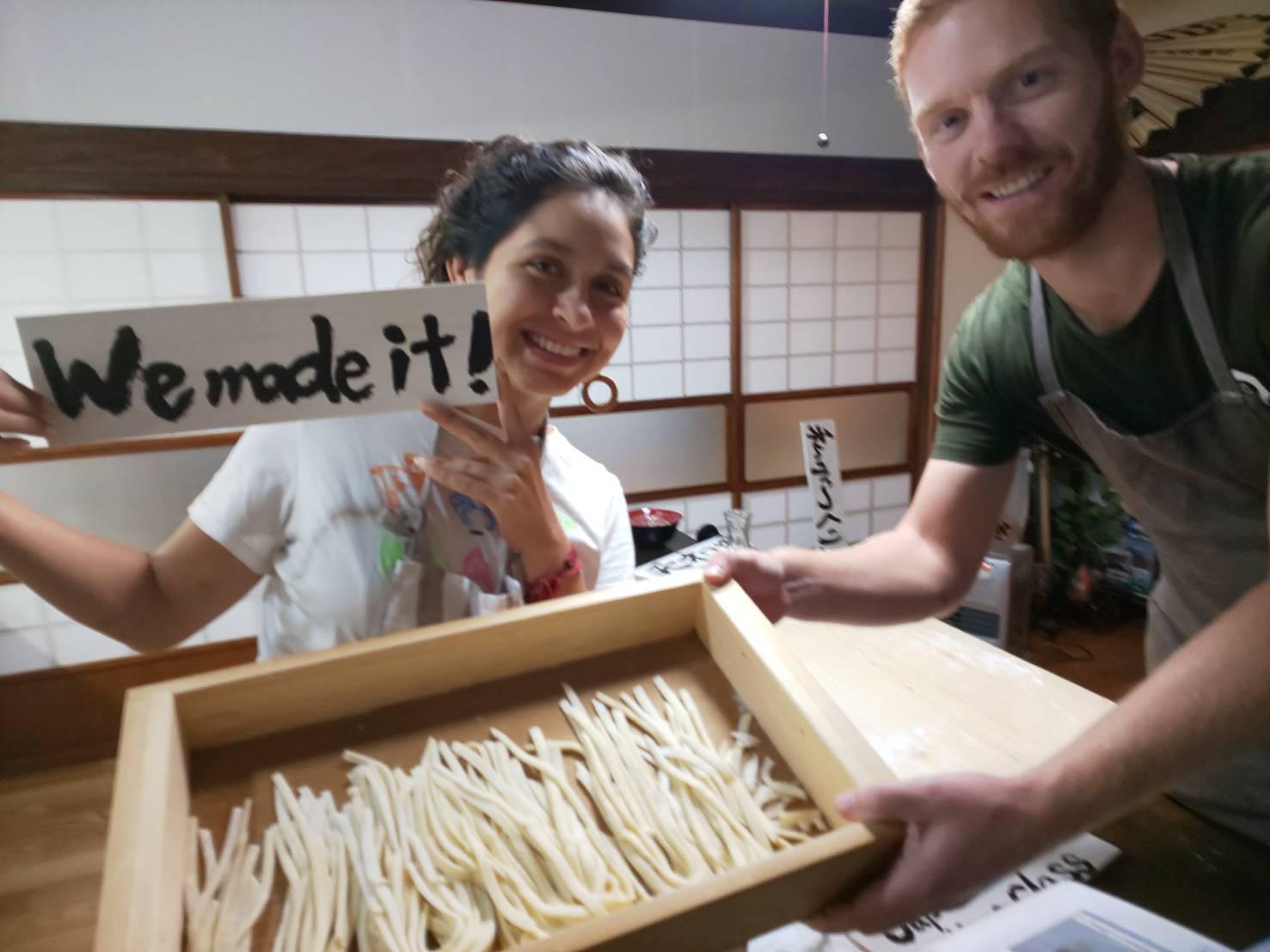 Two people holding a tray of hoto noodles that they made