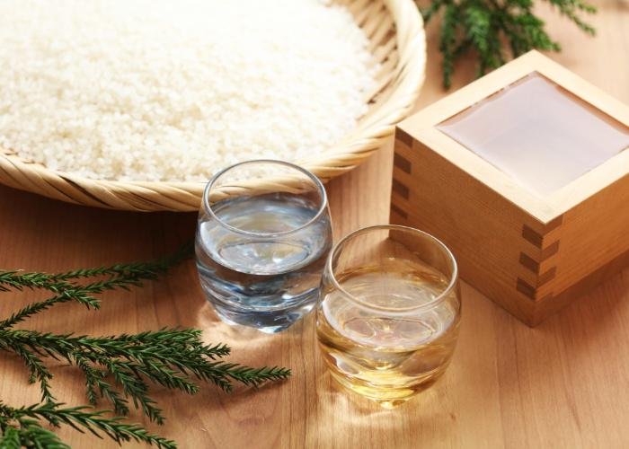 Two glasses of Japanese sake next to a wooden tray of rice