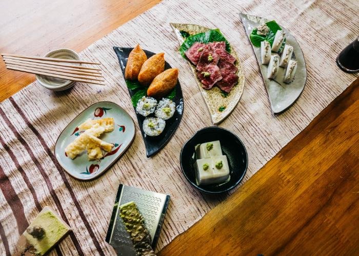 An overhead shot of several dishes paired with Japanese wasabi: sushi rolls, tempura, fish cakes, and more
