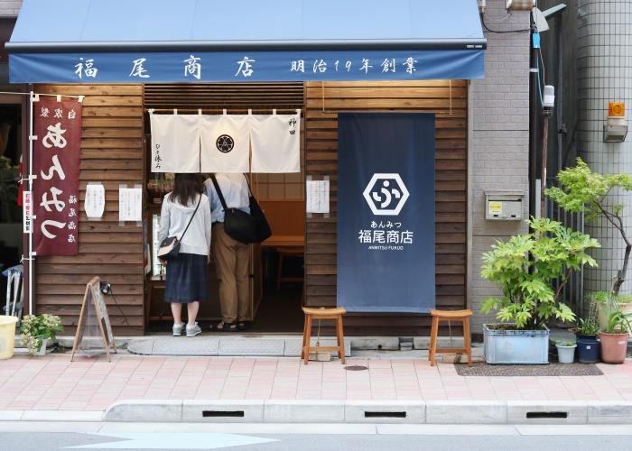 Two people stand under the noren of a Japanese anmitsu shop