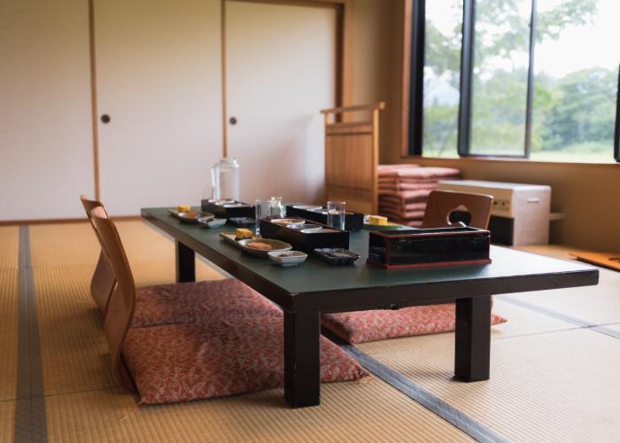 A traditional ryokan inn room with a low table and chairs on tatami mat flooring.