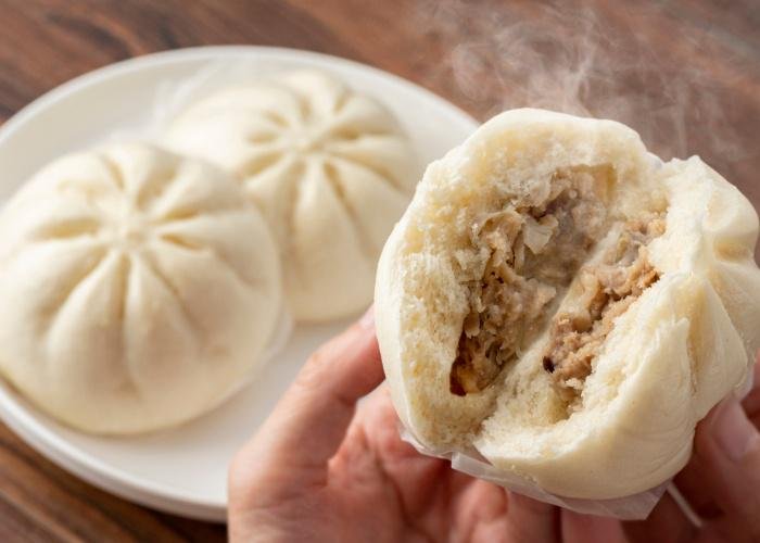 Japanese nikuman, a plate of steamed buns and close up of hands breaking a steamed bun in half