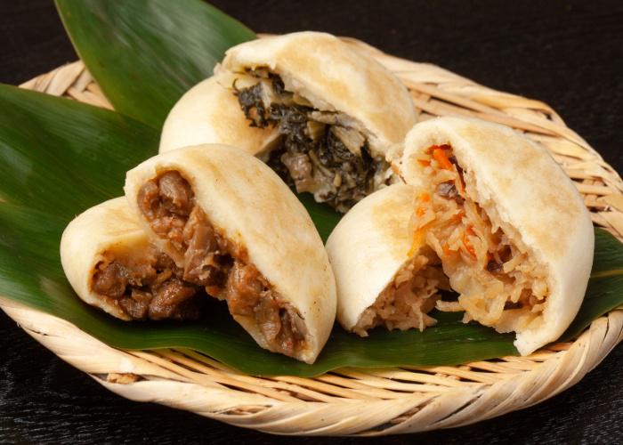 Three types of oyaki, Nagano's specialty dumplings, filled with various fillings like veggies and meat, on a bamboo platter