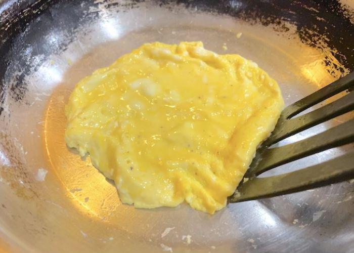 Soft scrambled eggs in frying pan with spatula